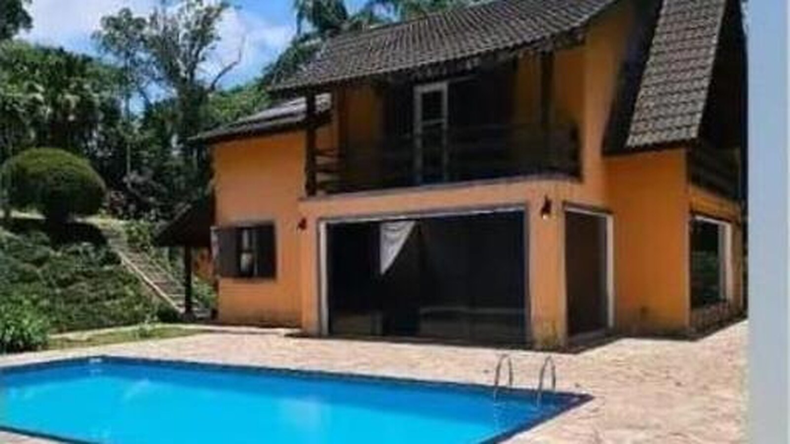 Área da piscina com casa laranja ao fundo e vegetação